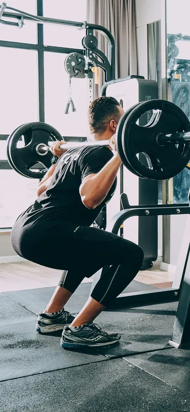 A lifter at the bottom of a barbell back squat, seen from behind and to one side (stock photo).